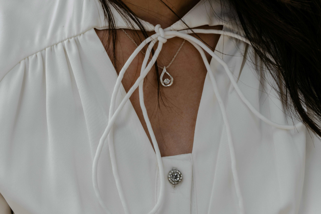 Close-up of woman wearing white blouse with tie neckline and silver teardrop pendant necklace with gemstone detail